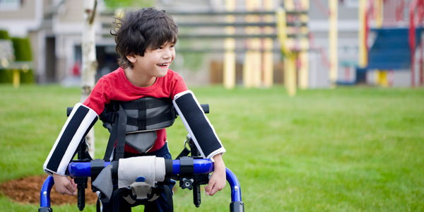 A smiling child with cerebral palsy using a walker outdoors