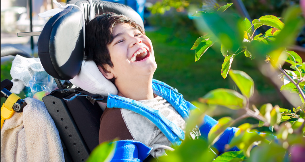 A smiling child using a wheelchair outdoors